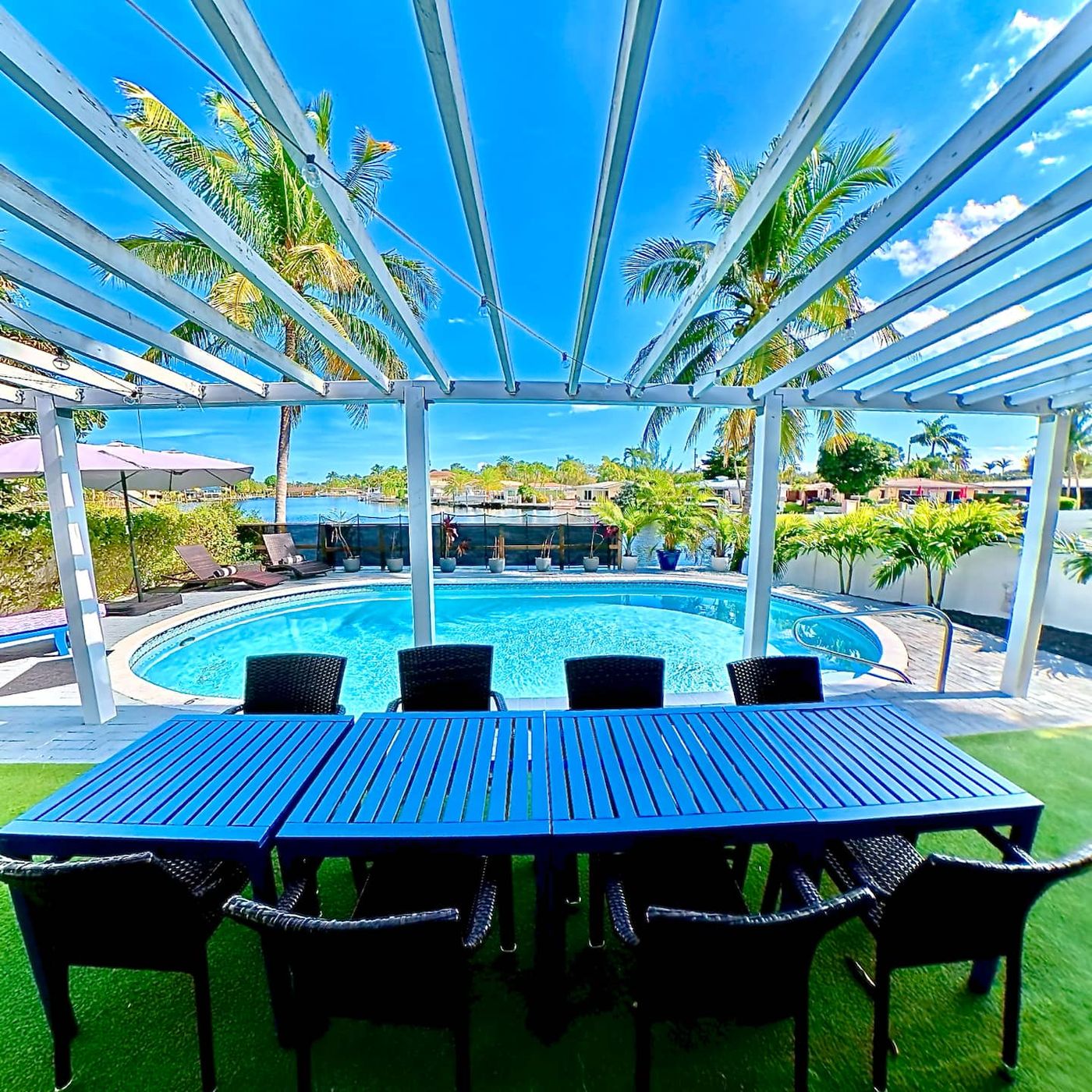 Long dinner table set under the pergola beside the pool